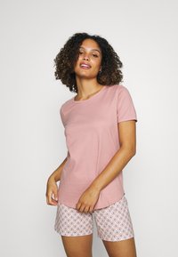 Zachtroze t-shirt met korte mouwen gecombineerd met lichte, gestippelde shorts met een bloemenpatroon in blauwe en koraalkleurige accenten.