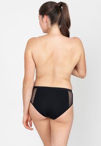 Zwarte bikini onderkant met gaas zijpanelen, zachte stof en een high-waisted ontwerp. De achteraanzicht benadrukt de snit en textuur.