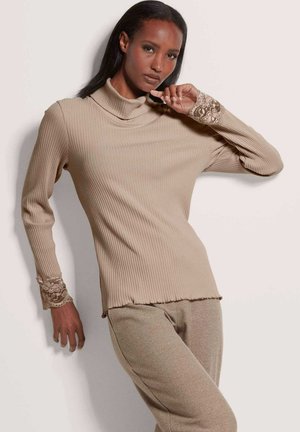 Beige geripptes Rollkragenshirt mit langen Ärmeln, das Spitzenakzente an den Bündchen aufweist. Der Saum ist leicht ausgefranst, was dem Design Textur verleiht.