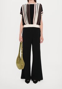 Svarta vida byxor i kombination med en flerfärgad randig blus. En grön mockaväska och svarta klackar fulländar looken.