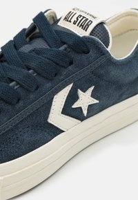 Zapatillas de ante azul marino con detalles en crema, un logotipo de estrella y un diseño texturizado en la lengüeta. Suela de goma con un ligero tacón.
