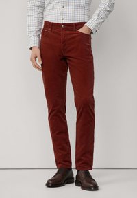 Rote Cordhosen mit schmaler Passform, fünf Taschen, Frontknopfverschluss und feiner Textur. Kombiniert mit braunen Lederschuhen.