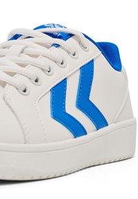 Weißer Schuh mit blauen Akzenten, mit einem glatten synthetischen Obermaterial, runder Zehenform und kontrastierenden blauen Streifen. Dicke weiße Sohle mit strukturiertem Profil.