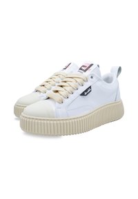 White sneakers with cream-colored rubber soles, round toe, and textured accents. Features beige laces and logo detail on the sides.