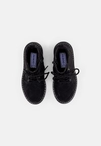 Czarne buty na sznurówki z wzorzystą strukturą, z bocznymi zamkami błyskawicznymi i białymi szwami wzdłuż podeszwy. Wewnątrz widoczne niebieskie logo.