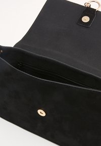 Svart mockaväska med öppet lock, visar invändig dragkedjeficka och magnetisk tryckknapp i guldton.