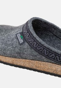 Grå slip-on sko med sort mønstret trim, korksål og "StepMan" stofmærke på siden.