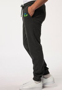 Donkergrijze joggers met zakken, elastische tailleband en verstelbaar trekkoord. Voorzien van meerkleurige tekst "EAST IRON BAY" aan de voorkant.