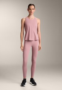 Pink sleeveless top paired with matching pink leggings. The fabric has a smooth texture. Black athletic shoes complete the outfit.