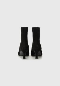 Bottines en daim noir avec un talon élancé, dotées d'une fermeture éclair sur le côté et d'une texture lisse, conçues pour une silhouette ajustée.