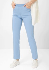 Lichtblauwe stretchpants met een brede elastische tailleband, zijzakken en taps toelopende pijpen, gecombineerd met witte sneakers.