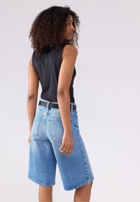Denimshorts i lys vask med høj talje, med fem lommer og synlige sømme. Sat sammen med en sort ærmeløs top.