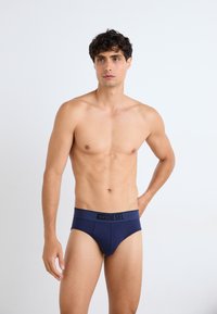 Marineblaue Herrenunterhosen mit einem dunklen Bund, auf dem der Markenname "DIESEL" in Schwarz steht. Der Stoff wirkt glatt und dehnbar.