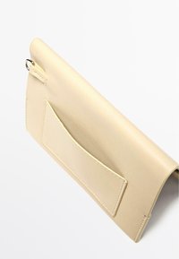 Beżowa skórzana kopertówka o gładkiej fakturze, prostokątnym kształcie i przedniej kieszeni. Z metalowym pierścieniem i ozdobnymi przeszyciami.