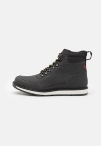 Botas de cuero negras hasta el tobillo con punta redonda, sistema de cordones circular y suela de goma blanca. Presentan un logotipo en el lateral y una pestaña para tirar.