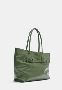 Groene leren totebag met twee handvatten en decoratieve riemdetail aan de voorkant, geplaatst tegen een effen witte achtergrond.