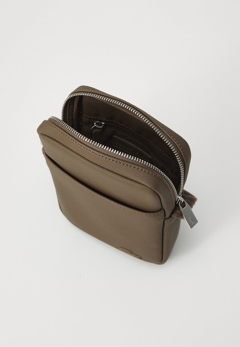 Sac bandoulière en nylon marron avec zip et poche frontale unique. Présente une texture lisse et des accents en métal argenté.