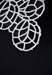 Biała koronkowa tkanina z motywem liści przedstawia skomplikowane, okrągłe i wydłużone kształty na czarnym tle.