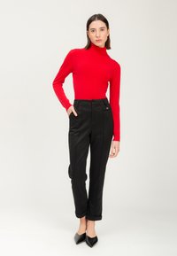 Rode coltrui gecombineerd met zwarte broeken. De broek heeft zijpiping en opgerolde manchetten. Het model draagt spitse zwarte hakken.