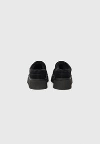 Pantofi negri slip-on cu un exterior din suede texturat și căptușeală din blană sintetică, având o talpă groasă din cauciuc negru și un toc rotund.