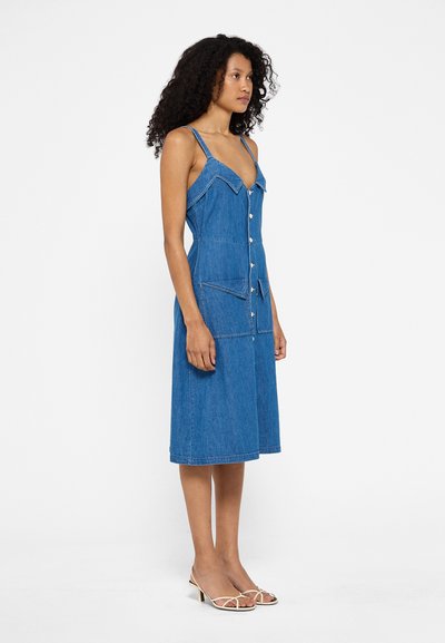 Denim midi kleita ar regulējamām siksnām, pogu aizdari un divām priekšējām kabatām. Gaiši zila krāsa ar kontrastējošiem šuvju elementiem.