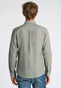 Camicetta verde a maniche lunghe con texture, colletto button-down, caratterizzata da pieghe posteriori e orlo arrotondato, abbinata a jeans blu casual.