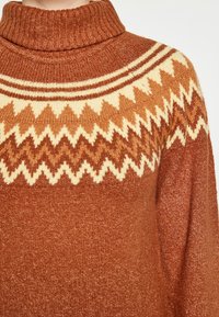 Tömény barna garbó pulóver, krém és világosbarna cikkcakk mintával a mellkasán, textúrált kötött anyagból.