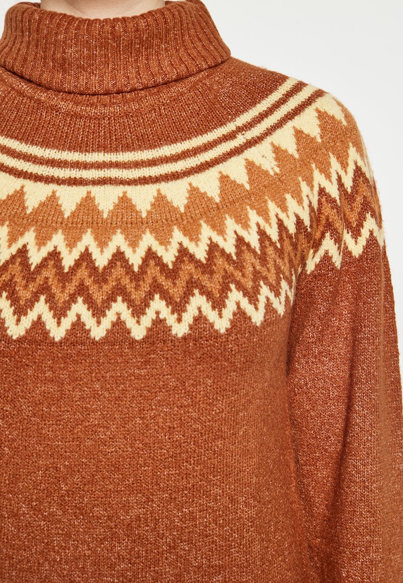 Tömény barna garbó pulóver, krém és világosbarna cikkcakk mintával a mellkasán, textúrált kötött anyagból.