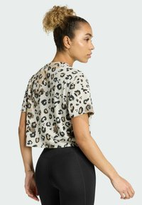 Top corto e a maniche corte in un beige chiaro con un motivo a stampa leopardata nera e marrone, realizzato in tessuto morbido, abbinato a leggings neri.