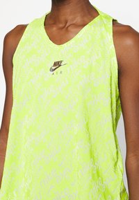 Svetle zelené bezrukávové tílko s opakovaným logem Nike, lehký materiál a výstřih do V s malým logem Nike v přední části.