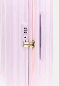 Valigia rigida rosa con scanalature verticali, accessori dorati, lucchetto a combinazione a manopola e una cerniera. Manico integrato sul lato.