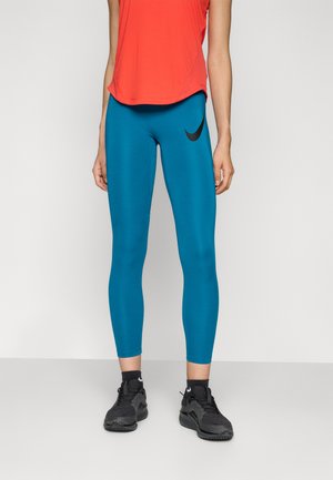 Plave tajice s crnim Nike logom, uparene s crvenom sportskom majicom i crnim tenisicama. Tajice su uske i glatke.