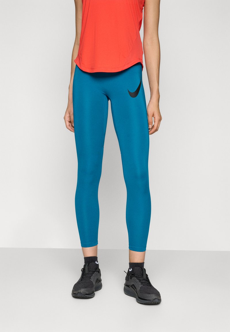 Leggings bleus avec un logo Nike noir, associés à un t-shirt de sport rouge et des baskets noires. Les leggings sont ajustés et lisses.