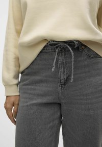 Felpa color beige chiaro abbinata a pantaloni in denim grigi con vita regolabile. Il tessuto ha una consistenza sottile e una vestibilità comoda.