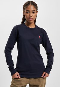 Granatowy t-shirt z długim rękawem, wykonany z bawełny, z okrągłym dekoltem i małym, czerwonym logo na piersi. Gładka tekstura z dopasowanymi rękawami.