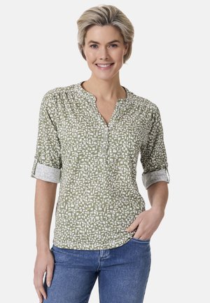 Grüne Bluse mit einem weißen geometrischen Muster, Dreiviertelärmel und Rundhalsausschnitt. Hellgraue Akzente an den Ärmeln.