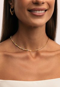 Collana in oro con perle multicolori, tra cui rosa, verde, arancione e bianco, esposta su una clavicola.