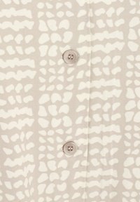 Tissu beige clair avec des taches abstraites blanches irrégulières et deux boutons beiges cousus le long d'une couture centrale.