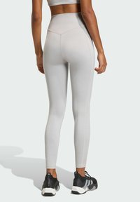 Light gray high-waisted leggings with a smooth texture and fitted design, featuring a seam detail along the backside and paired with black sneakers.