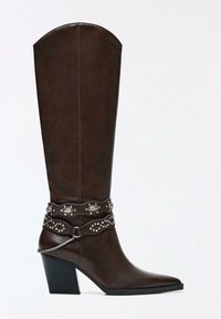 Bruine nep leren kniehoog laars met een spits toelopende neus, een gestructureerde schacht, een decoratieve zilveren ketting en studs rond de enkel, en een dikke hak.