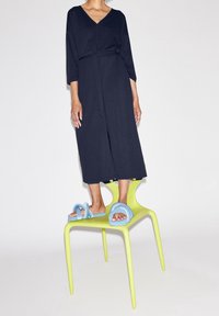 Granatowa sukienka dżersejowa z dekoltem w serek, ściągniętym w pasie i rękawami do trzech ćwiartek, zestawiona z jasnoniebieskimi, masywnymi sandałami na zielonym krześle.