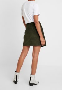 Olivgrön kordflors minikjol med ett åtsittande midja, i kombination med en vit t-shirt med kort ärm och grå ankle boots med ormskinnsmönster.