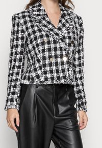 Svart- och vitrutigt tweedjacka med dubbelknäppt design, spetsiga slag och metallknappar, tillsammans med svarta läderbyxor.