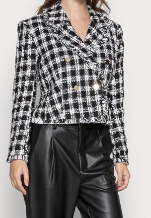 Giacca in tweed a quadri bianco e nero con design doppiopetto, rever a punta e bottoni metallici, abbinata a pantaloni in pelle nera.