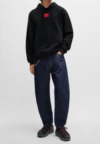 Sweat à capuche noir avec un logo rouge, jean denim bleu ample, et baskets noires avec des accents rouges. Comprend une poche kangourou et des cordons de serrage.