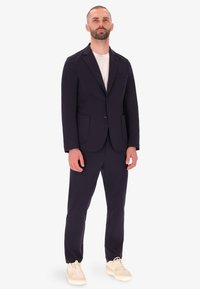 Set giacca e pantaloni blu navy, in misto cotone, chiusura a singolo bottone, rever a punta, tasche frontali, abbinato a una t-shirt bianca e sneakers beige.