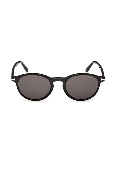 Lunettes de soleil rondes noires avec des verres foncés, une monture fine et un logo "T" blanc sur chaque branche près des charnières.