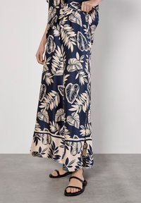 Falda maxi de flores azul marino con patrones de hojas color crema, abertura lateral, tela ligera, combinada con sandalias planas negras.