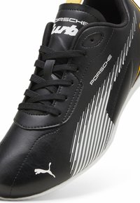 Černá syntetická bota s bílými a žlutými akcenty, štíhlý design, texturovaný povrch a výrazné logo Puma na boku.