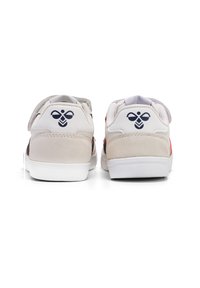Białe sneakersy z połączeniem gładkich i zamszowych tekstur, z czerwonym akcentem i granatowym logo na pięcie. Rzep na jednym bucie.